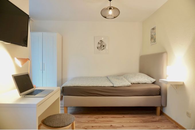 Ein modernes Schlafzimmer mit einem Doppelbett, Schreibtisch und Fernseher, ideal für Entspannung und Arbeit.