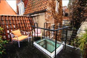 Dachterrasse mit modernen Stühlen und Glasboden, umgeben von Ziegelmauern und Pflanzen, ideal für städtische Wohnräume.