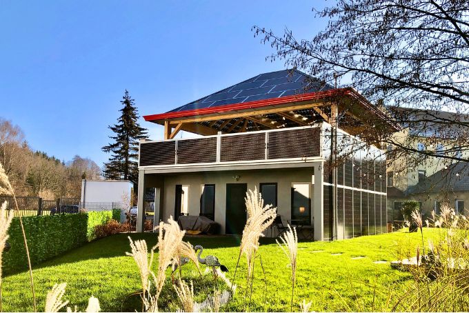 Moderne Villa mit Solaranlage auf dem Dach und grünem Garten, umgeben von Pflanzen und einem gepflegten Außenbereich.