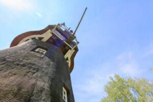 Historische Windmühle mit Holzstruktur und grünen Bäumen im Vordergrund, ideal für Architektur- und Landschaftsfotografie.