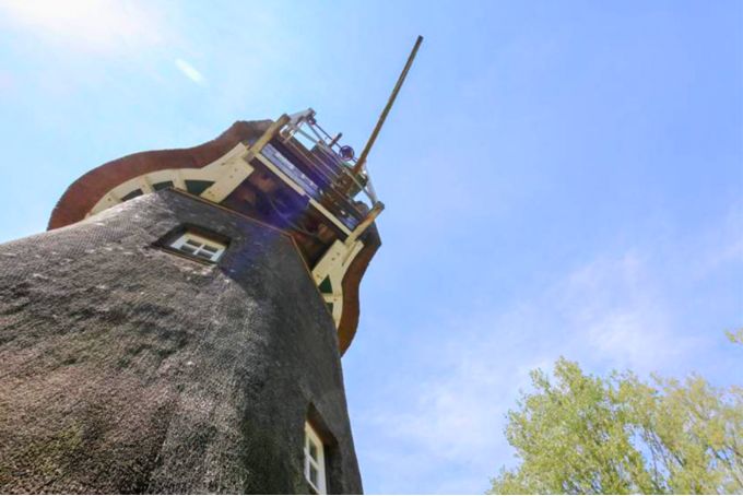 Historische Windmühle mit Holzstruktur und grünen Bäumen im Vordergrund, ideal für Architektur- und Landschaftsfotografie.