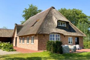 Traditionelles Haus mit Reetdach und Ziegelmauer, umgeben von Grünflächen und einem gepflegten Garten.