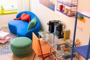 Bunte Wohnzimmereinrichtung mit blauer Couch, grüner Pouf und Kaffeemaschine auf einem Tisch, ideal für moderne Wohnräume.