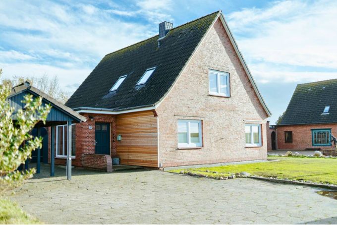 Einfamilienhaus aus Ziegel mit Holzverkleidung, zwei Fenstern und einem Garten, ideal für Familien. Sicht auf die Fassade und den Eingang.