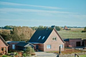 Ein modernes Einfamilienhaus mit einem Satteldach in ländlicher Umgebung, umgeben von Bäumen und Feldern.