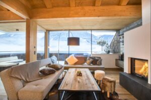 Gemütliches Wohnzimmer mit Holzdetails, Sofa, Tisch und Kamin, ideal für entspannte Abende in den Bergen.