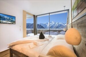 Schlafzimmer in einer modernen Berghütte mit Blick auf die Berge und eine große Fensterfront.