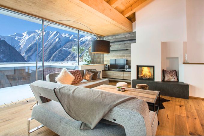 Helle und moderne Wohnlandschaft mit gemütlicher Couch, Kamin und Blick auf die Berge durch große Fenster.