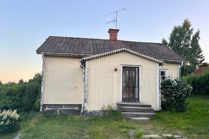 Eine kleine, gelbe Holzhütte mit einem Eingang und einem Schornstein, umgeben von Grün und Pflanzen, ideal für ländliche Szenen in Schweden