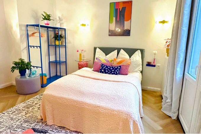 Ein modernes Schlafzimmer mit einem Bett, bunten Kissen, einem Regal und Pflanzen, ideal für stilvolle Wohnräume.